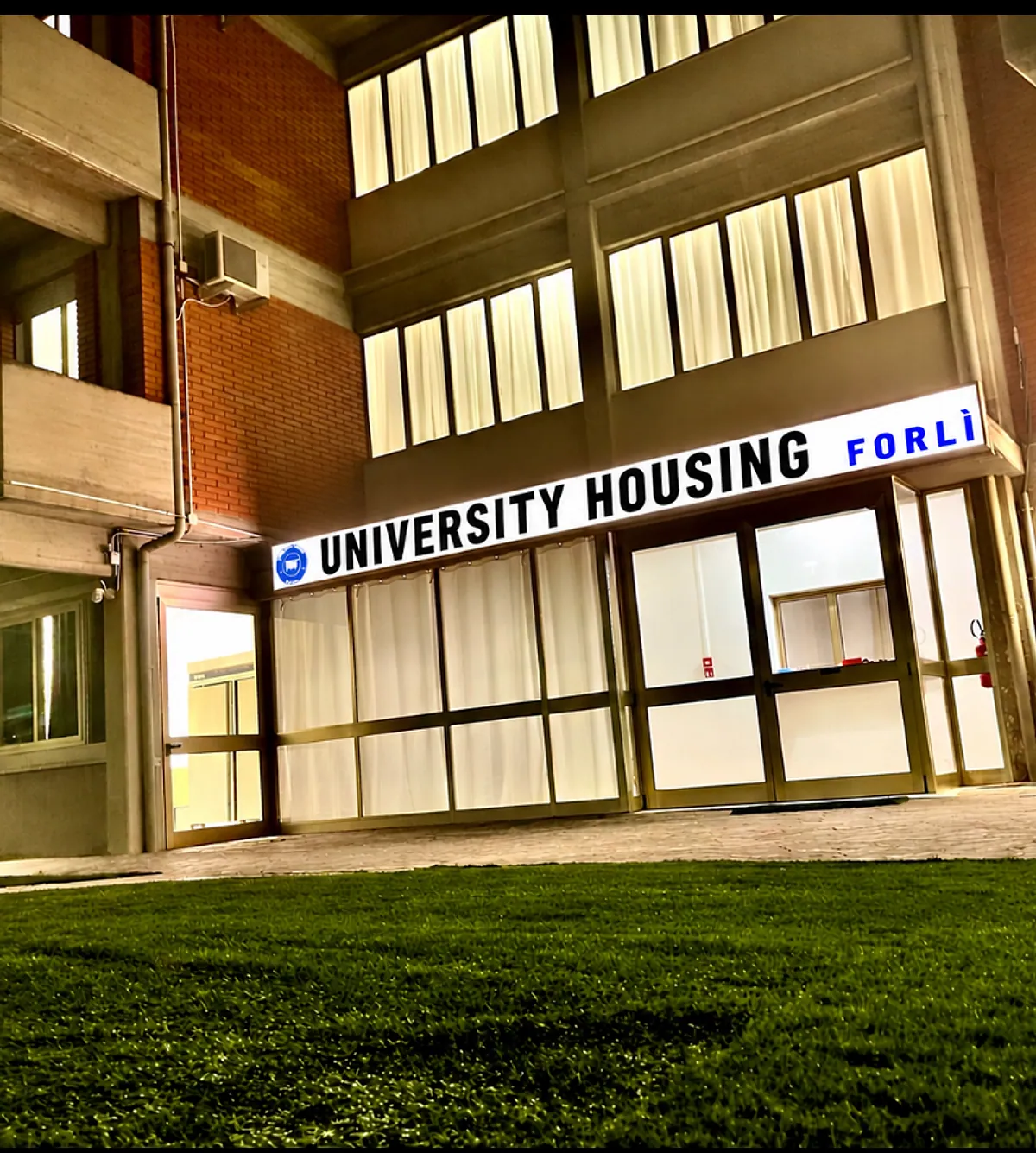 L’ingresso della residenza di sera, con l’insegna University Housing Forlì